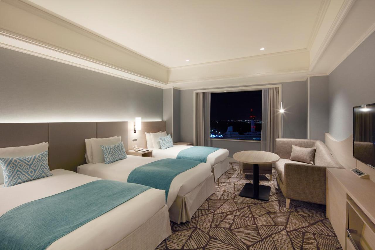 Grand Nikko Tokyo Daiba Hotel Exterior photo The photo shows a modern hotel room featuring two twin beds, each adorned with turquoise bed runners. The room has light gray walls and a stylish decor that includes a small table and a chair. Large windows let in natural light and offer a view, like