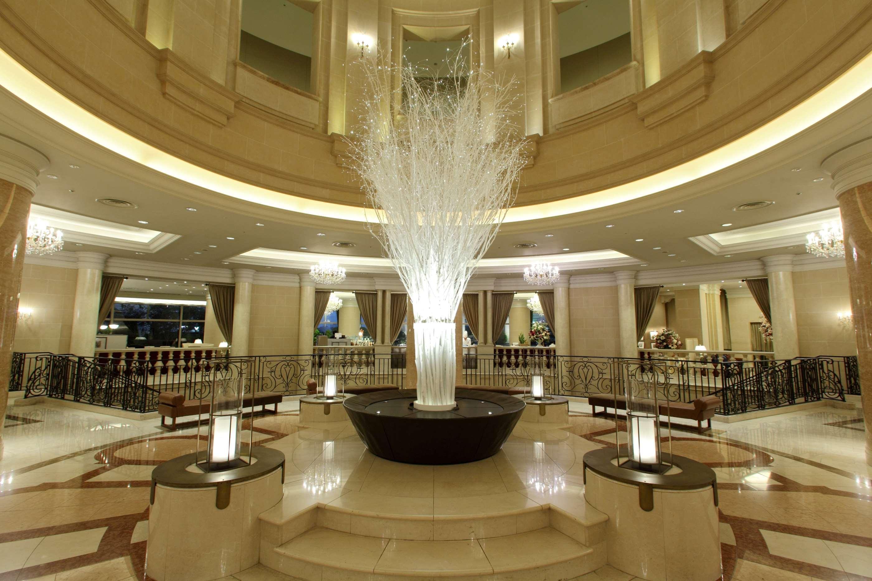 Grand Nikko Tokyo Daiba Hotel Exterior photo The photo shows an elegant hotel lobby with a grand circular design. In the center, there is a large decorative arrangement that resembles a tree or plant, made of white materials, set in a sleek black base. Surrounding this centerpiece are several l